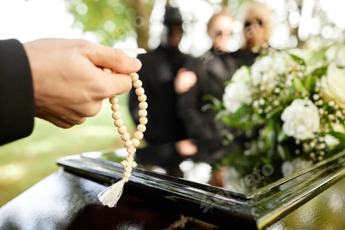 Preview: Man holding rosary and praying at outdoor funeral