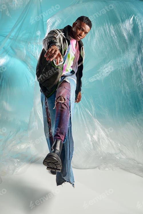 Preview: Full length of trendy young afroamerican model in outwear jacket and ripped jeans