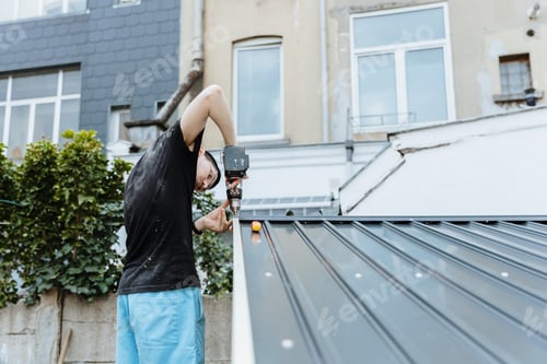Preview: A worker guy installs a roof on a metal shed with a screwdriver.