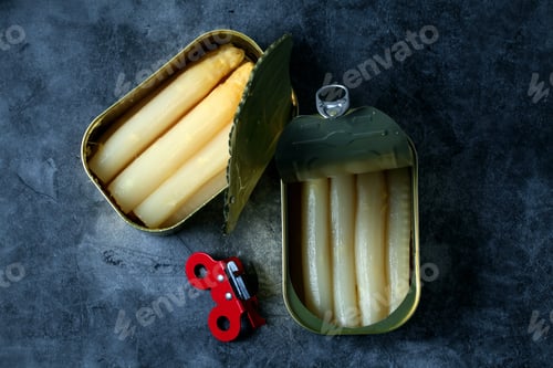 Preview: Top view of asparagus in cans with a red can opener isolated on a dark-gray ceramic surface