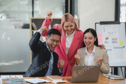 Preview: Joyful asian business team celebrating success with raised hands in office.