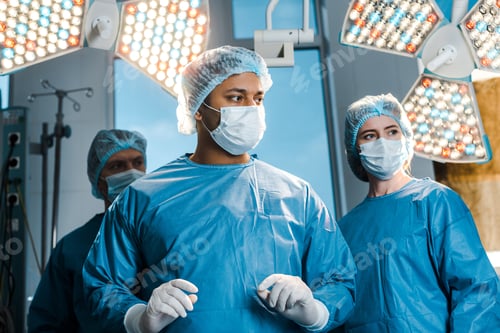 Preview: doctors and nurse in uniforms and medical masks looking away in operating room