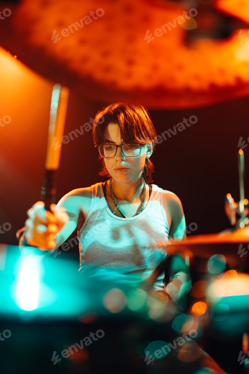 Preview: Female drummer performing live on stage with drumsticks and illuminated background