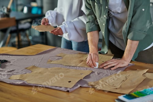 Preview: Cropped view of craftsman marking cloth near sewing patterns and blurred african american colleague