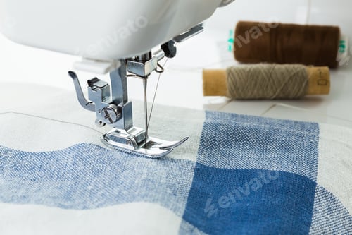 Preview: Sewing a blue checkered fabric with spools of thread nearby in a bright workspace