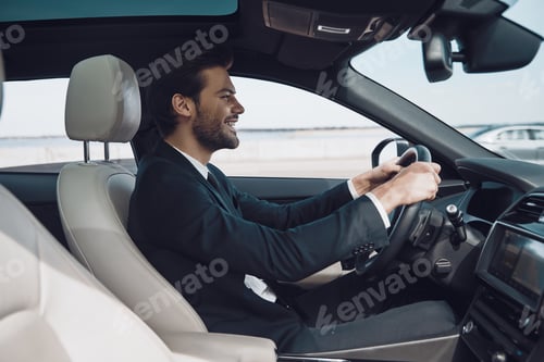 Preview: In love with high speed. Handsome young man in full suit smiling while driving a car