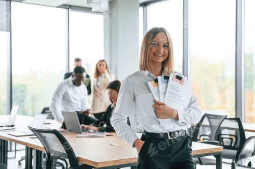 Preview: Happy woman is standing in front of her colleagues. Group of office workers are together indoors