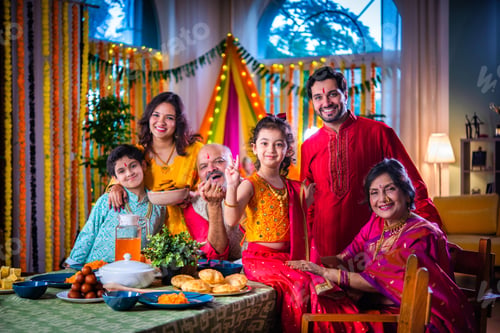Preview: Portrait of happy Indian family in traditional outfit celebrating Diwali at home eating food