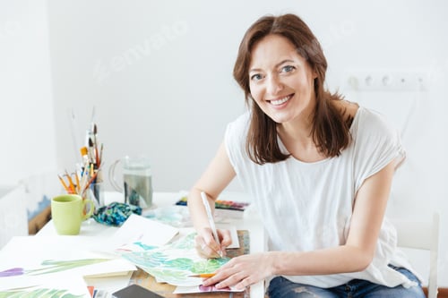 Preview: Cheerful woman artist sitting and drawing in art studio