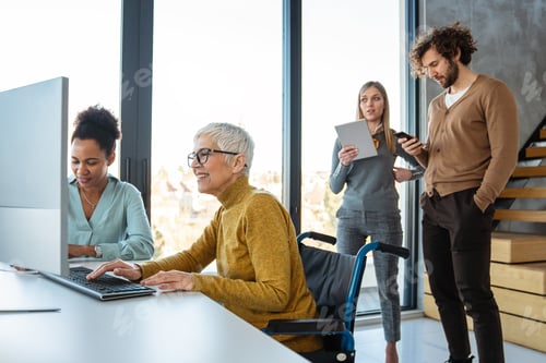 Preview: Business woman in wheelchair working with colleague in modern inclusive office. Diversity, support