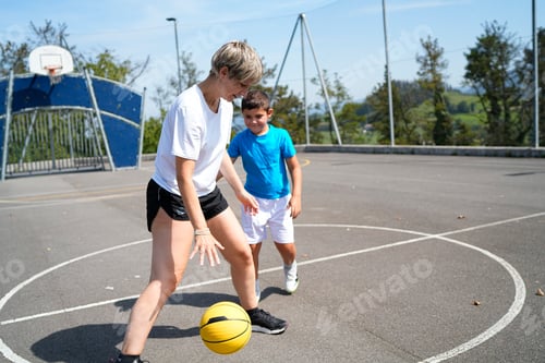 Preview: Mother teaching her son how to dribble a basketball on an outdoor court
