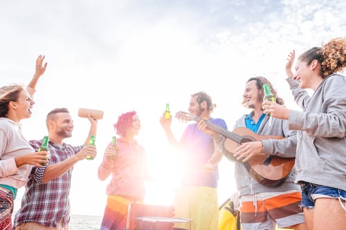 Preview: Happy friends drinking beers and playing guitar at barbecue on the beach
