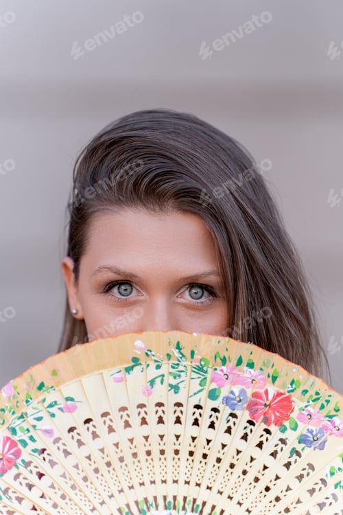Preview: Woman hiding face behind a hand fan.