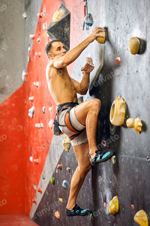 Preview: Male climber exercising in gym, climbing up on artificial wall with boulders.