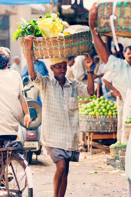 Preview: A man carrying a large basket of bananas on his head in a busy marketplace.