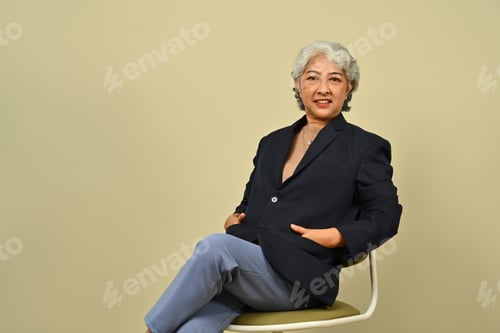 Preview: Beautiful mature business woman in black suit with confident smile posing over beige background.