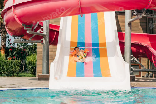 Preview: Child boy laughing while slide in pool after going down water slide at sunny day in water Aqua park