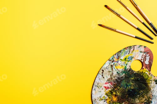 Preview: Top View of Paintbrushes And Palette With Brushstrokes on Yellow Surface