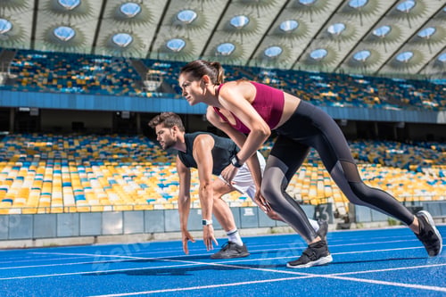 Preview: athletic young male and female sprinters in start position on running track at sports stadium