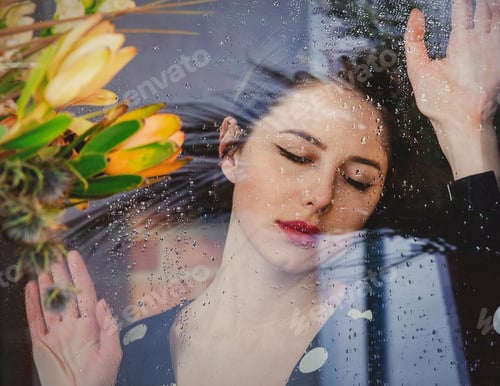 Preview: woman at the wet window after the rain misses the plants standing outside the window.