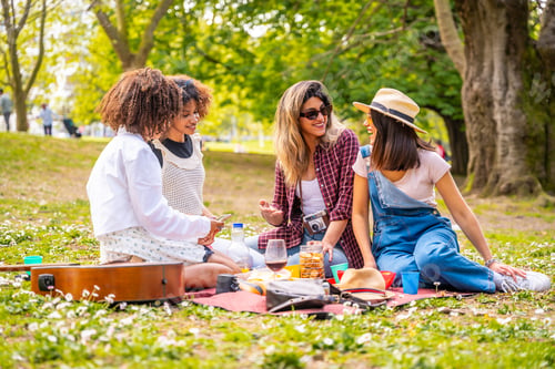 Preview: Cheerful friends enjoying picnic, relaxing on blanket in park during spring day