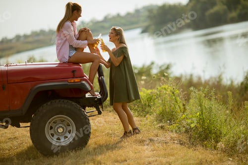Preview: Two young women having fun on hood of a red car