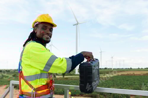 Preview: Portrait of smart engineer with protective helmet at electrical turbines field