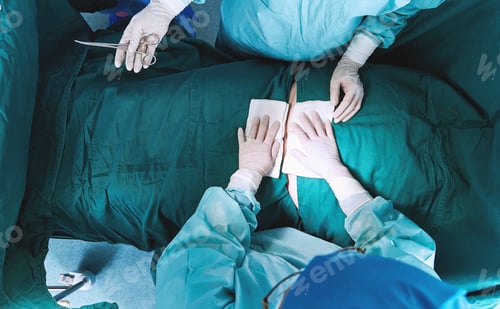 Preview: Overhead view of surgeons performing operation on abdomen in maternity ward operating theatre