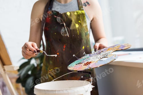 Preview: Close-up view of young inspired girl working with painting knife and palette in light studio