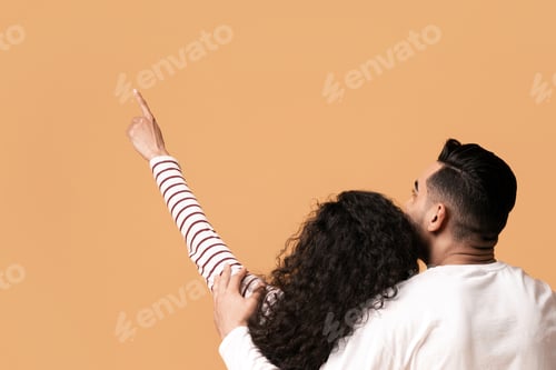 Preview: Young couple embracing and pointing up while sitting on floor, rear view