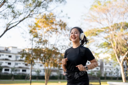 Preview: Asian woman in sportswear listening to music in headphone while running jogging exercising in park.