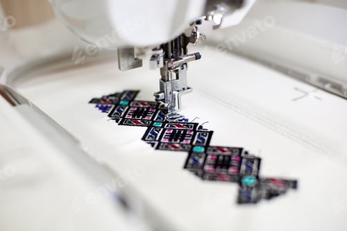 Preview: Close-up of sewing machine creating colorful abstract geometrical pattern on white fabric.
