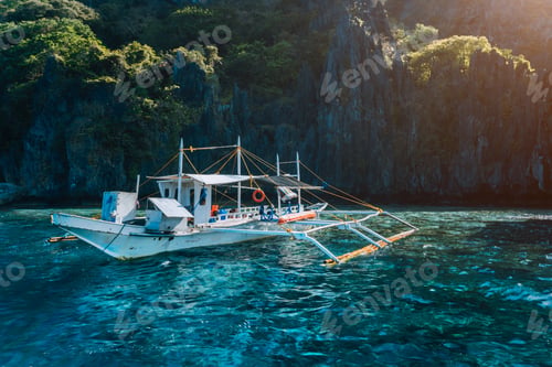 Preview: Banca local boat on turquoise water against huge limestone cliffs. Island hopping tour trip