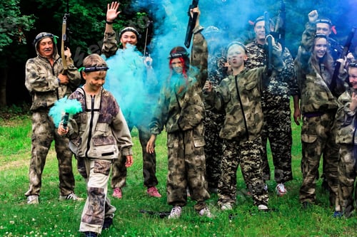 Preview: People in camouflage celebrating winning laser tag shooting game with colored smoke. N