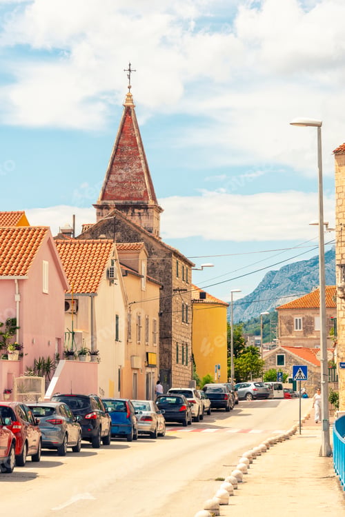 Preview: Narrow street lined with cars and colorful buildings with picturesque view of Makarska
