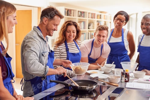 Preview: Male Teacher Making Pancake On Cooker In Cookery Class As Adult Students Look On