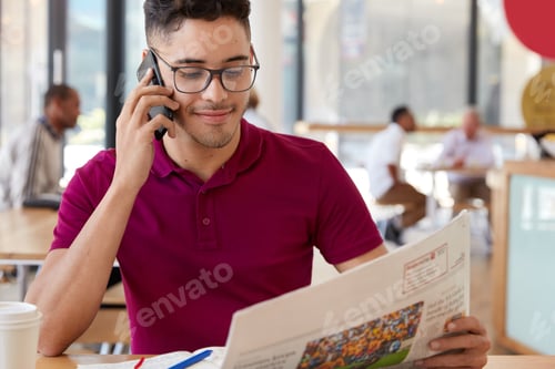 Preview: Horizontal shot of handsome pleased male model reads morning news in newspaper, talks via cellular,