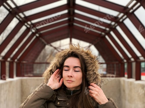 Preview: Portrait of a young woman in winter clothes on brown geometric city architecture