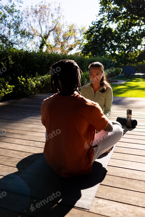 Preview: Happy diverse couple practicing yoga sitting on deck smiling in sunny garden, copy space