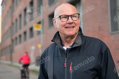 Preview: Portrait of a smiling senior man with eyeglasses waiting at a bus stop in the city