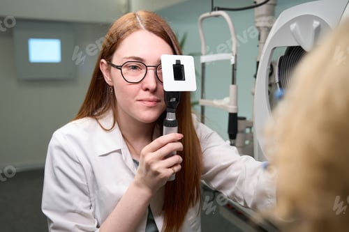 Preview: Red-haired ophthalmologist checks the eyes of a patient
