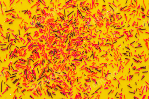 Preview: Top view of red and black sweet sprinkles on yellow background
