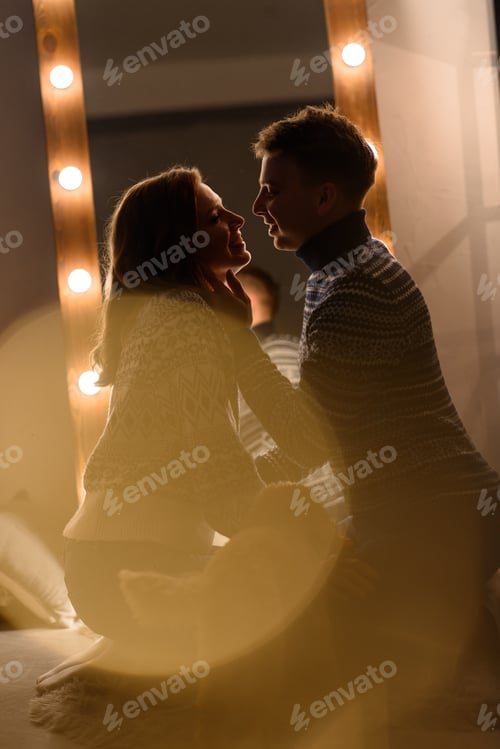 Preview: A couple in love in knitted sweaters sit on their knees in front of each other.