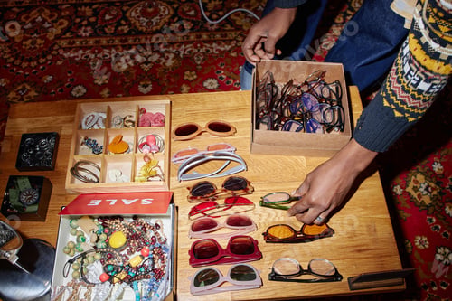 Preview: Young Adult Black Man Selecting Second Hand Sunglasses at Vintage Market Table
