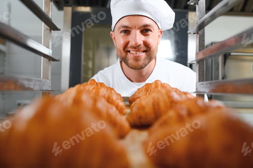 Preview: Smiling baker holding tray with fresh cooked croissants in bakehouse