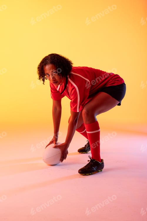 Preview: Portrait of african american female rugby player with rugby ball over neon yellow lighting