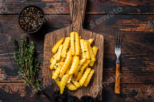 Preview: Baked Crinkle French fries potatoes sticks or chips on a wooden board.