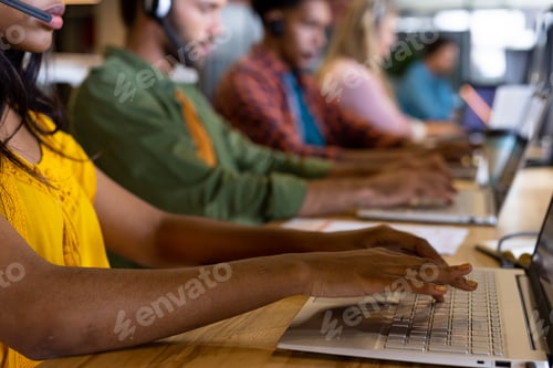 Preview: Diverse male and female creative colleagues working using computers and phone headsets in office