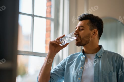 Preview: Thirsty man having a glass of water at home.