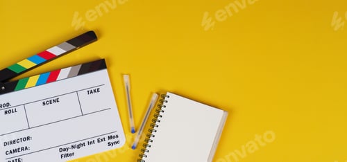 Preview: Clapper board with notebook and pens on yellow background.